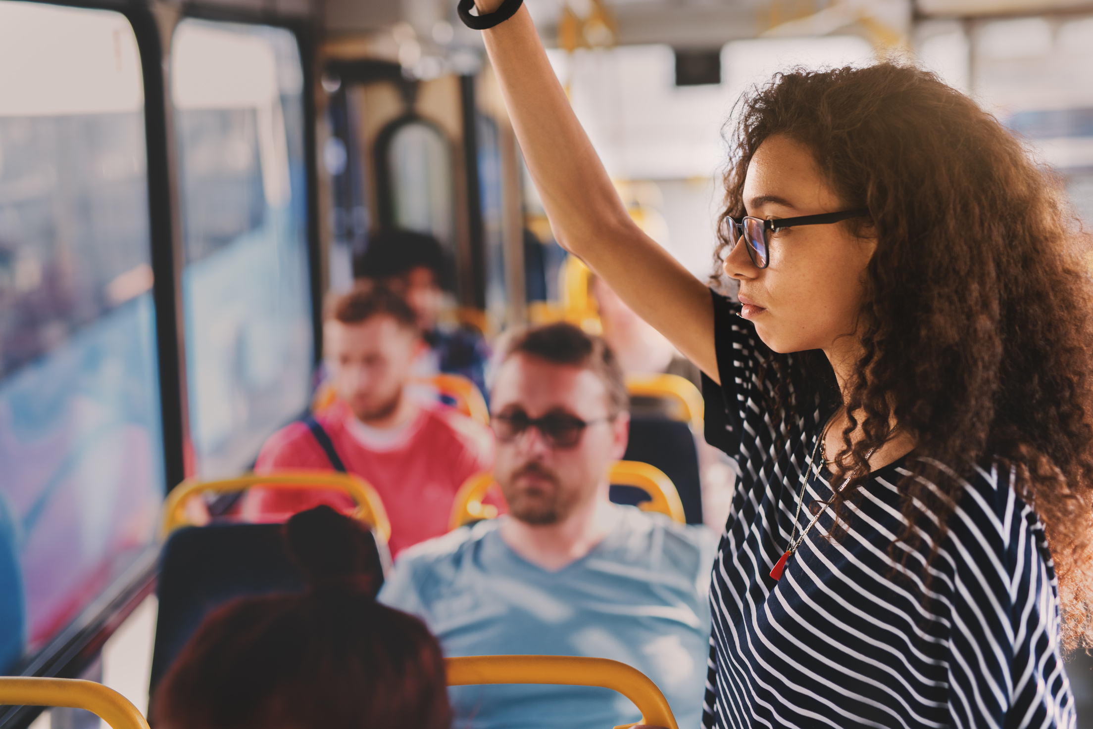 Serious young curly girl standing in a bus full of people.